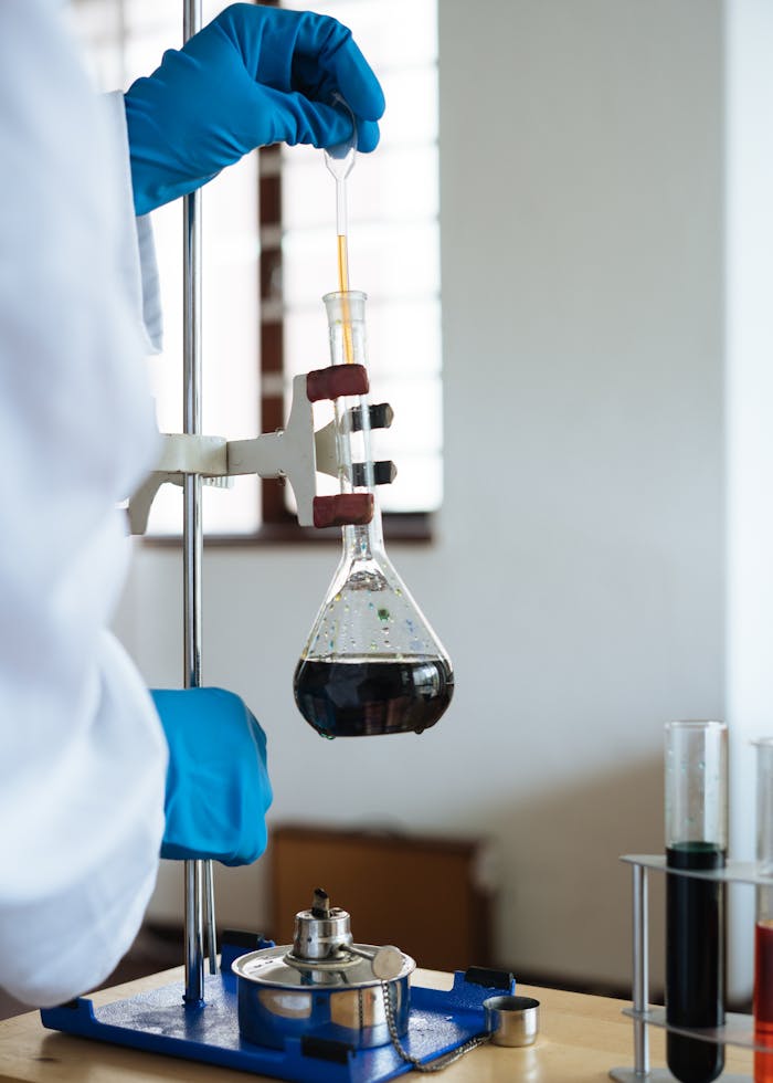 Scientist using pipette and flask in laboratory experiment, wearing gloves.